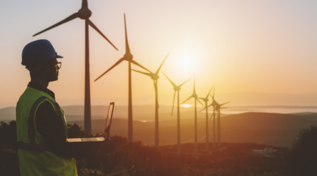 Wind farmer holding computer at sunset